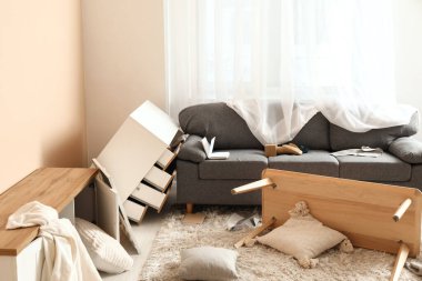 Depremden sonra dağınık mobilyalarla aydınlık oturma odası.