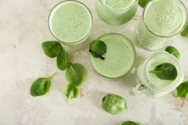 Bardaklar ve mason kavanozu beyaz masada taze ıspanaklı smoothie.