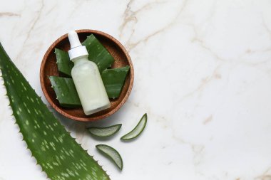 Aloe vera yaprağı, ahşap kase ve mermer arka planda gerekli yağ şişesi.