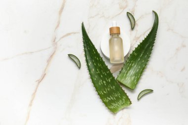 Taze aloe yaprakları ve gerekli yağ şişesi mermer arka planda duruyor.