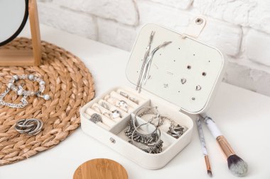 Beyaz tuğla duvarın yanındaki masada farklı takılarla dolu bir kutu, yakın plan.