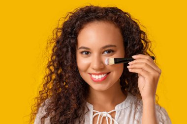 Sarı arka planda fırçası olan güzel, mutlu, Afro-Amerikalı bir kadın.