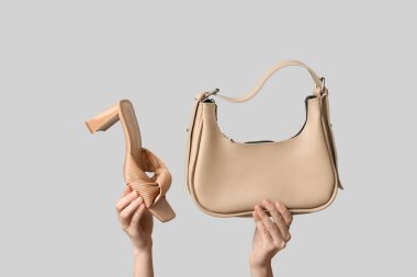 Gri arka planda kadın eli ve topuklu ayakkabı.