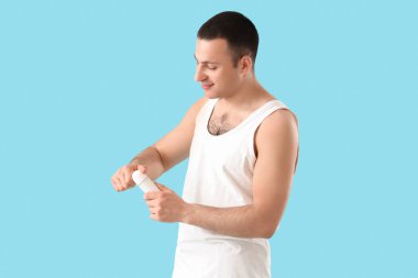 Mavi arka planda deodorantı olan yakışıklı bir genç.