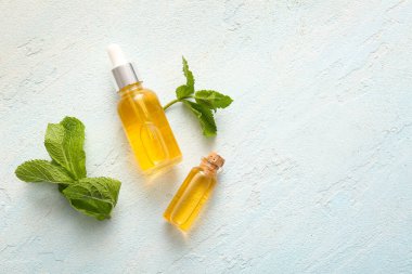 Esaslı nane yağı şişeleri ve soluk mavi arka planda yeşil yapraklar