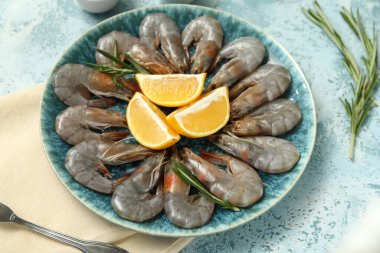 Mavi arka planda taze çiğ karides, limon ve biberiye tabağı.