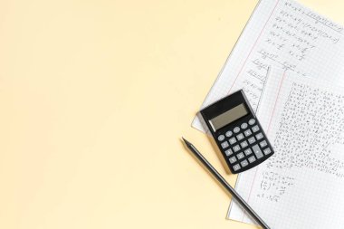 El yazısıyla yazılmış matematik formülleri, kalem ve hesap makinesi içeren metin kitabı sarı arkaplanda