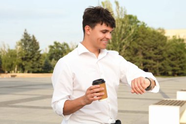 Bir fincan lezzetli latte ile yakışıklı genç adam dışarıda zamanı kontrol ediyor