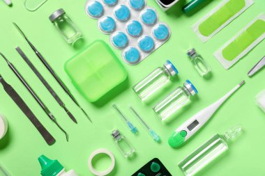 Termometresi, hapları ve neşteri olan tıbbi malzemeler yeşil arka planda. Üst görünüm