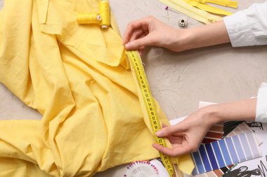 Gri arka planda kumaş ölçen kadın terzinin elleri. Üst görünüm