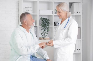 Nabız oksimetresi olan olgun bir adam ve klinikte doktor.