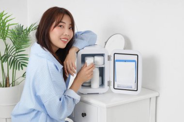 Evinde kozmetik ürünleri olan küçük buzdolabı olan güzel genç bir kadın.