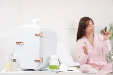 Kapalı küçük buzdolabı, kavanozlar ve kozmetik ürünleri evdeki masada, yakın plan.