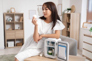 Güzel genç bir kadın ve evde kozmetik ürünleri olan küçük bir buzdolabı.