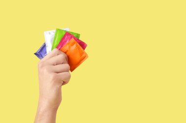 Sarı arka planda farklı prezervatifleri olan bir erkek.