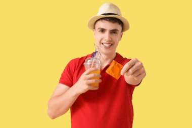 Sarı arka planda prezervatif ve kokteyl kullanan genç bir adam.