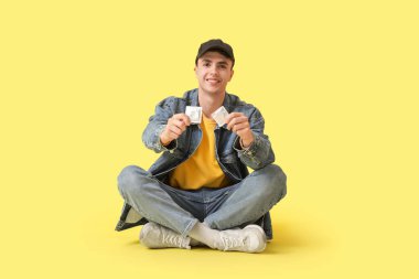 Lotus 'ta oturan genç adam sarı arka planda prezervatiflerle poz veriyor.