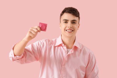Pembe arka planda prezervatif gösteren genç adam.