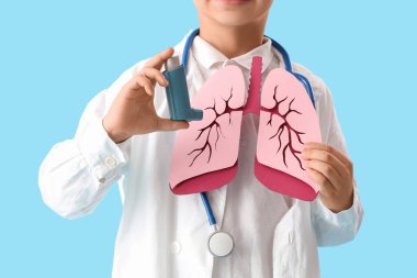 Kağıt ciğerli küçük doktor ve mavi arka planda astım spreyi, yakın plan.