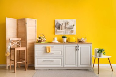 Sarı duvarda Peg tahtası ve mutfakta beyaz tezgah.