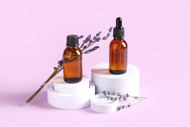 Eflatun arkaplanda kozmetik yağ şişeleri ve lavanta çiçekleri bulunan dekoratif podyumlar