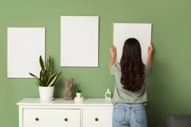 Evdeki yeşil duvara boş tuval asan genç bir kadın. Arka plan