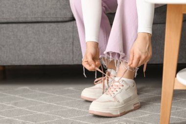 Şık ayakkabılı ve pembe pantolonlu bir kadın evde ayakkabı bağı bağlıyor.