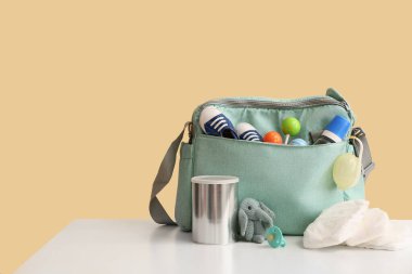 Bej arka planda emzik taşıyan bebek çantası