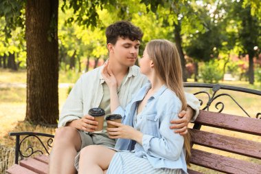Yaz parkında bankta oturan kahve fincanları olan güzel bir çift.