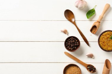 Tohumlu, biberli, fesleğenli ve sarımsaklı bir kase Dijon hardalı beyaz ahşap arka planda.