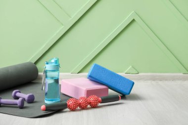 Spor şişesi, farklı ekipman ve yoga minderiyle yeşil duvarın yanında.