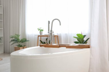 Modern banyonun içinde ahşap tepsiyle perdeli bir küvet.