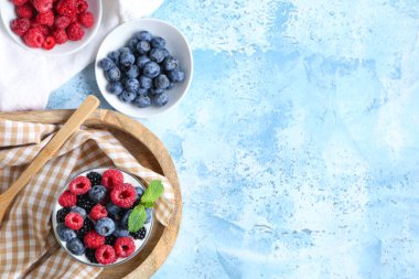 Farklı taze böğürtlenli ve açık mavi arkaplanda naneli bir bardak lezzetli yoğurt.