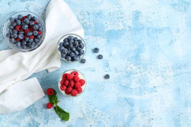 Taze yaban mersinli ve açık mavi arkaplanlı ahududu dolu bir bardak lezzetli yoğurt.
