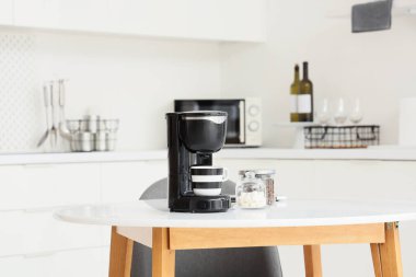 Mutfaktaki masada bir kavanoz kahve, şeker ve fincanlı modern makine.