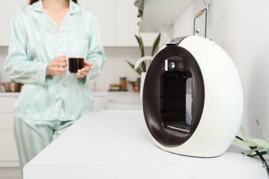 Bir fincan kahve ve modern makineli kadın mutfaktaki masada, yakın plan.