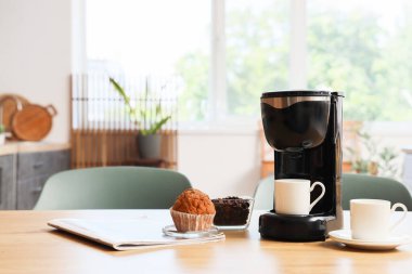 Mutfaktaki kahve makinesinde fincanlar, fasulyeler ve kekler var.