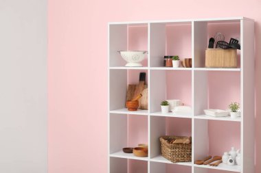 Mutfaktaki pembe duvarın yanında mutfak aletleri olan modern raf ünitesi.