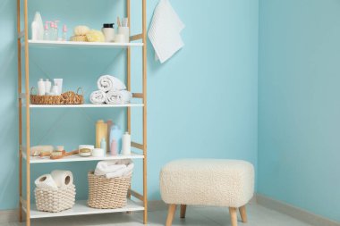 Banyo aksesuarları ve mavi duvarın yanında puf olan modern raf ünitesi.