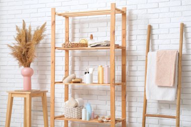 Banyo aksesuarları, otlar ve beyaz tuğla duvarın yanında merdiven olan modern raf ünitesi.