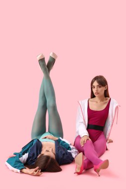 Pembe arka planda oturan şık elbiseli, güzel, genç, modaya uygun kızlar.