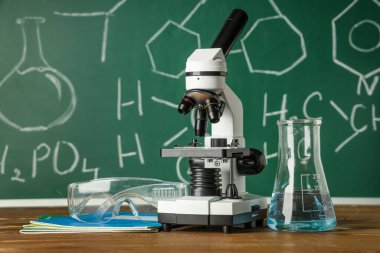 Modern mikroskop, koruyucu gözlükler ve kimyasal formüllü tahta masanın yanındaki matara.