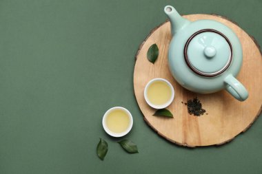 Yeşil arka planda kurumuş yapraklı sıcak çay kaseleri ve çaydanlık.