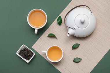 Yeşil arka planda kurumuş yapraklı çay fincanları ve çaydanlık.