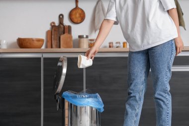 Mutfaktaki çöp kutusuna çöp atan kadın.