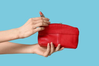 Kozmetik çantalı kadın elleri ve mavi arka planda ruj.