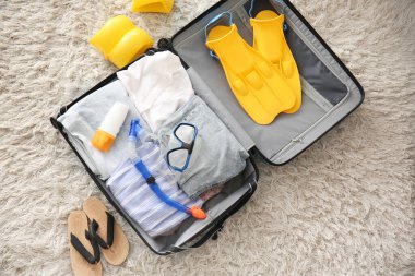 Oturma odasının zemininde giysi ve plaj aksesuarlarıyla dolu bir bavul. Yaz tatili kavramı