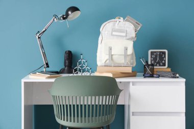 Mavi duvarın yanında lamba, saat ve okul çantası olan şık çocuk işyeri.