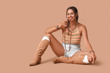 Kahverengi arka planda oturan Afrika kökenli Amerikalı güzel bir kadın.