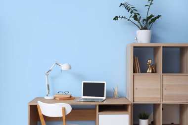 Dizüstü bilgisayarı, kitapları ve mavi duvarın yanındaki masa lambasıyla rahat çalışma alanı